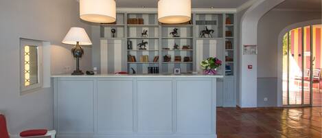 A spacious reception area with a central island, two pendant lights, a bookshelf, and a door with a frosted glass panel.