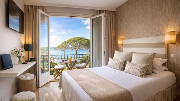 A hotel room with a large bed, a desk, a chair, a small table with a view, and a balcony with a table and chairs. - La Bastide du Port (Saint-Tropez)