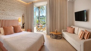 A hotel room with a bed, a sofa, a TV, and a balcony with a view of palm trees. - La Bastide du Port (Saint-Tropez)