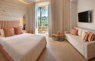 Une chambre d’hôtel avec un lit, un canapé, une télévision et un balcon donnant sur des palmiers.
