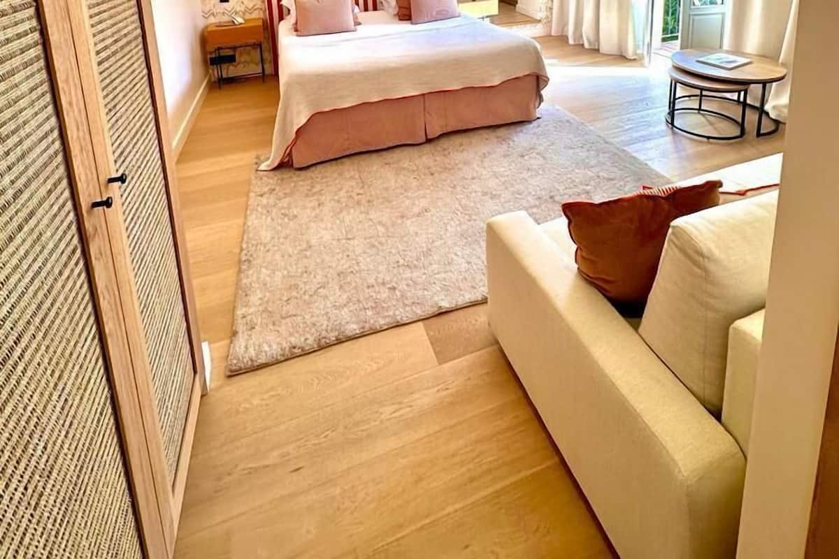 A modern bedroom with a large bed, a bedside table, a small table, and a view of greenery outside.