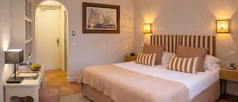 Un dormitorio con cama, mesitas de noche, lámpara, un cuadro enmarco y una puerta.