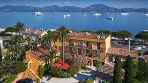 A coastal hotel with a view of the sea, featuring balconies, palm trees, and parked cars. - La Bastide du Port (Saint-Tropez)