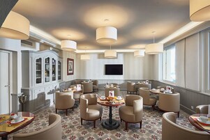 Un espace de restauration d’hôtel avec des tables rondes, des chaises et des luminaires suspendus.