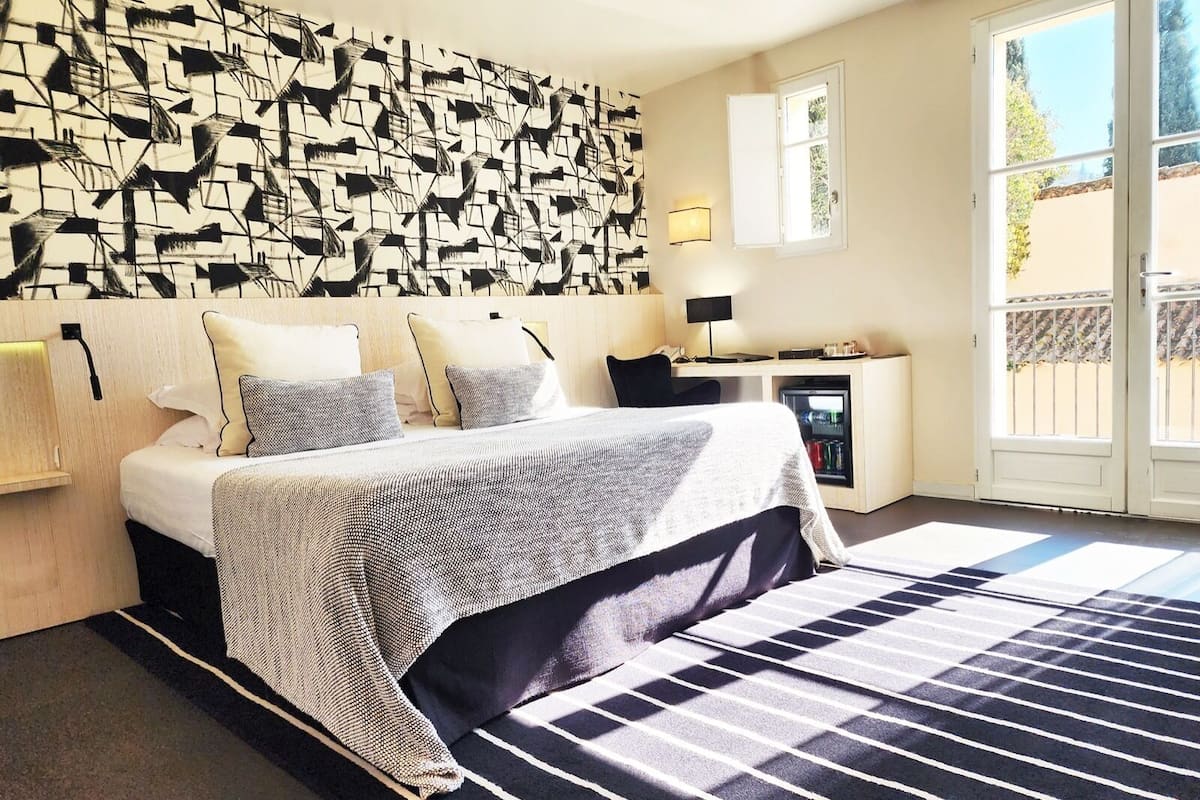 A hotel room with a bed, a desk, a refrigerator, and a window with a view of the outside.