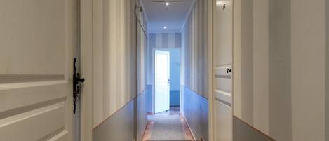 A hallway with white walls and doors, a carpeted floor, and a ceiling with recessed lighting.