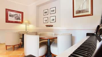 A dining area with a piano, four framed pictures on the wall, and a table with four chairs.