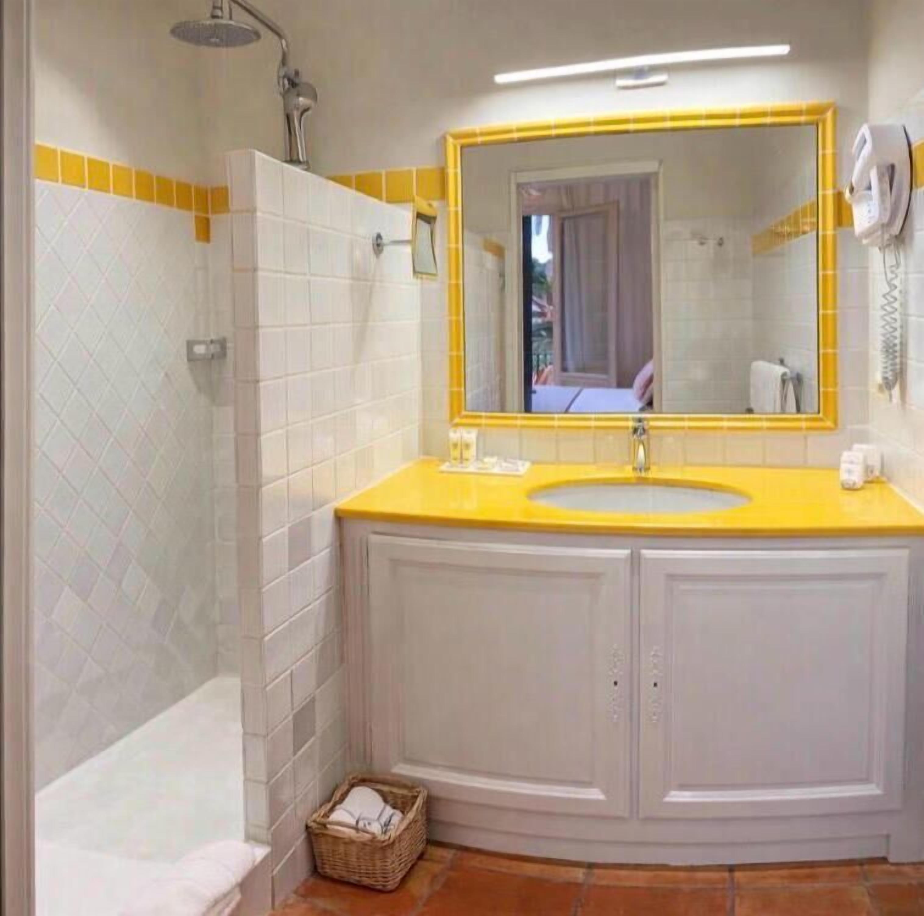 A bathroom with a yellow sink, white cabinets, a mirror with a yellow frame, and a shower.