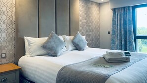 A neatly made bed with pillows, a bedside table, and a window with curtains.