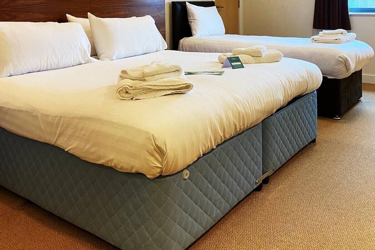 Hotellihuone, jossa on kaksi sänkyä, seinällä taulu ja ikkunassa verhot.