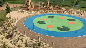 A playground with a circular play area, wooden structures, and a fenced perimeter.