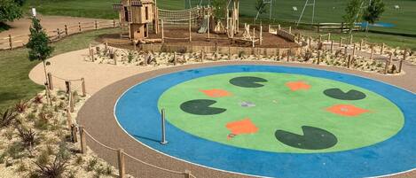 A playground with a circular play area, wooden structures, and a fenced perimeter.