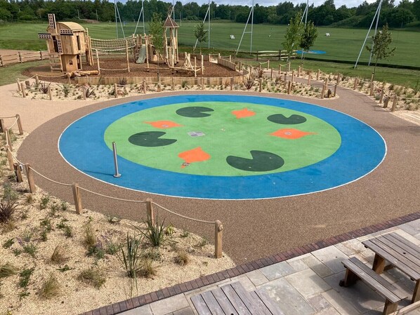Un parque infantil con una zona de juegos circular, estructuras de madera y una mesa de picnic.