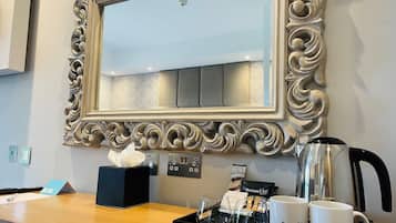 A hotel reception desk with a large ornate mirror, a coffee machine, and branded mugs.