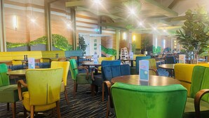 A modern restaurant with vibrant yellow and green seating, wooden tables, and green plants on the ceiling.