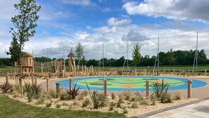 A playground with a fenced area, a wooden playhouse, and a small pavilion.