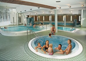 An indoor swimming pool with multiple lanes, a central hot tub area, and a tiled floor. - Holiday Club Salla Superior Apartments (Salla)