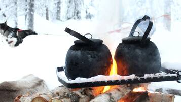 A campfire with two kettles on a metal rack, surrounded by snow-covered logs.