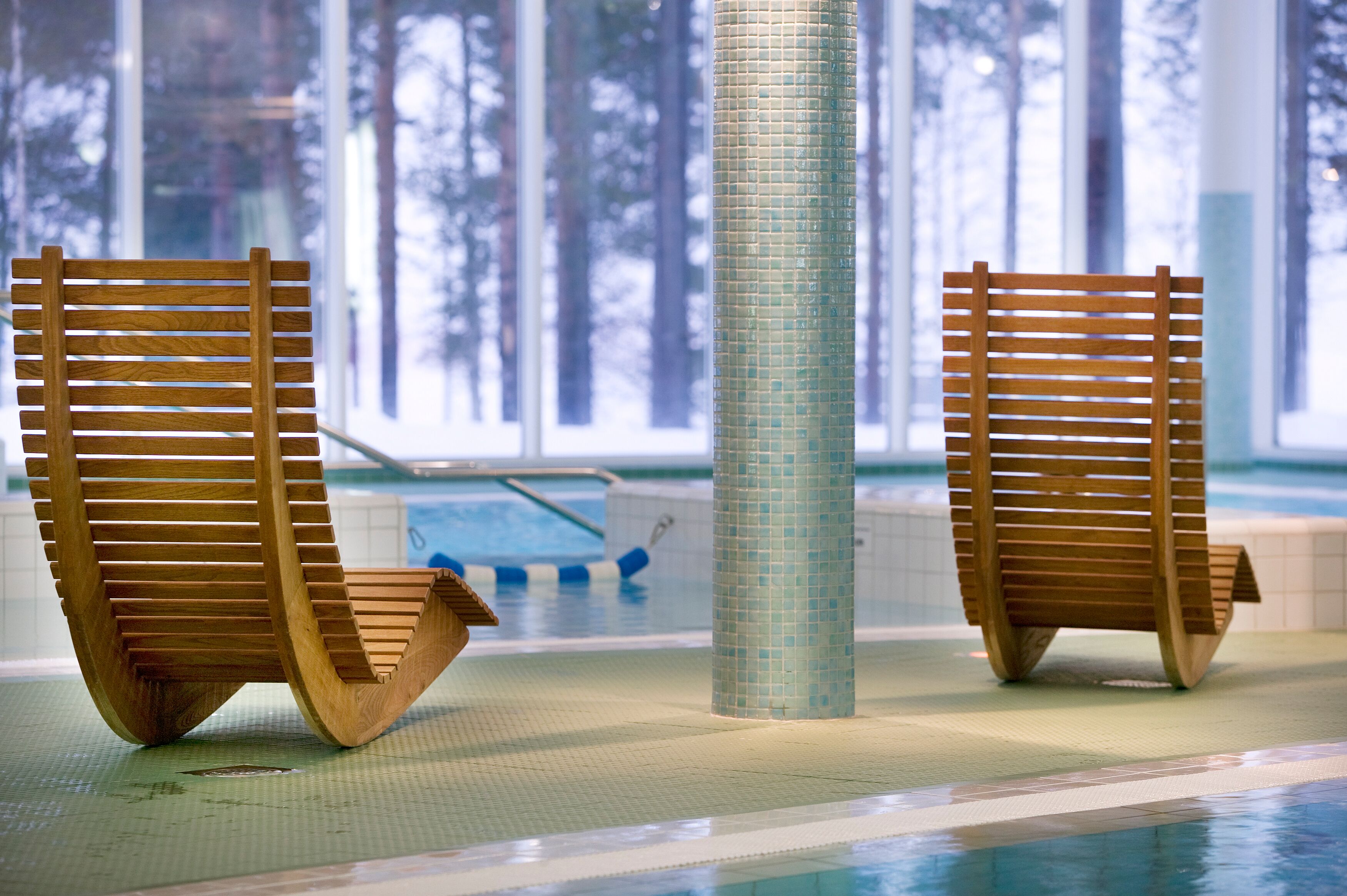 Two wooden chairs with slats leaning against a tiled column in a pool area.