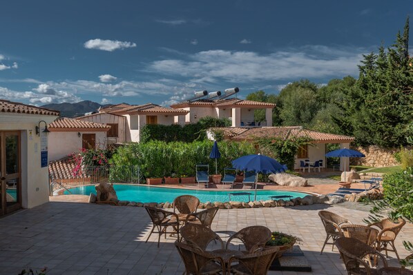 A pool area with lounge chairs, umbrellas, and a view of a mountain in the background.