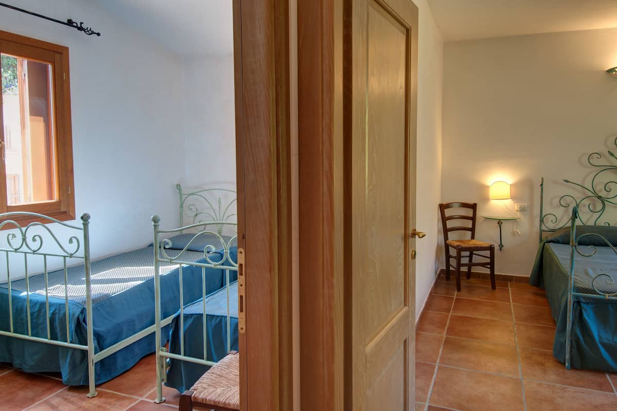Une chambre à coucher avec deux lits en métal, une porte en bois, une chaise et une lampe fixée au mur.