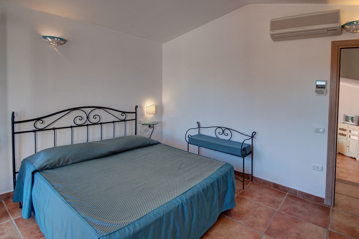 Une chambre à coucher comprenant un lit, une table de chevet, une lampe fixée au mur et un appareil de climatisation.