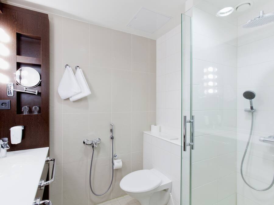 A modern bathroom with a glass-enclosed shower, a white toilet, and a vanity with a mirror and towel rack.