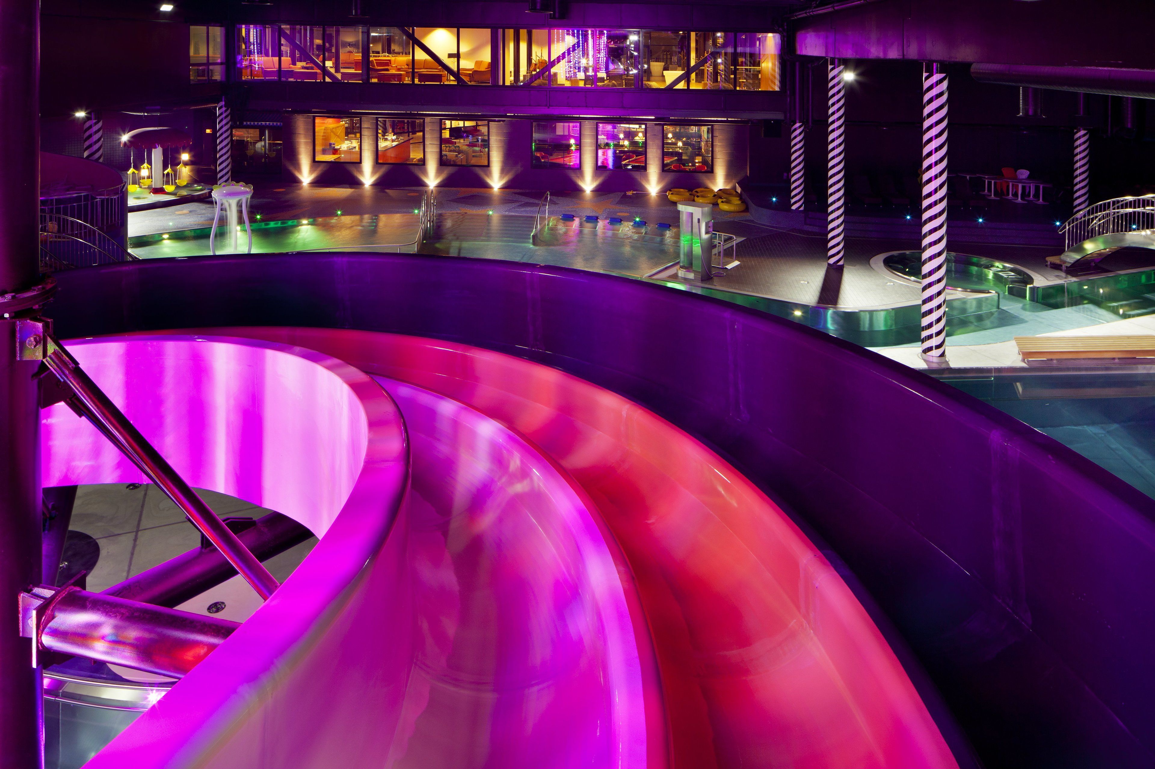 A modern indoor pool area with a central slide and surrounding seating.