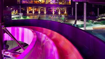 A modern indoor pool area with a central slide and surrounding seating.