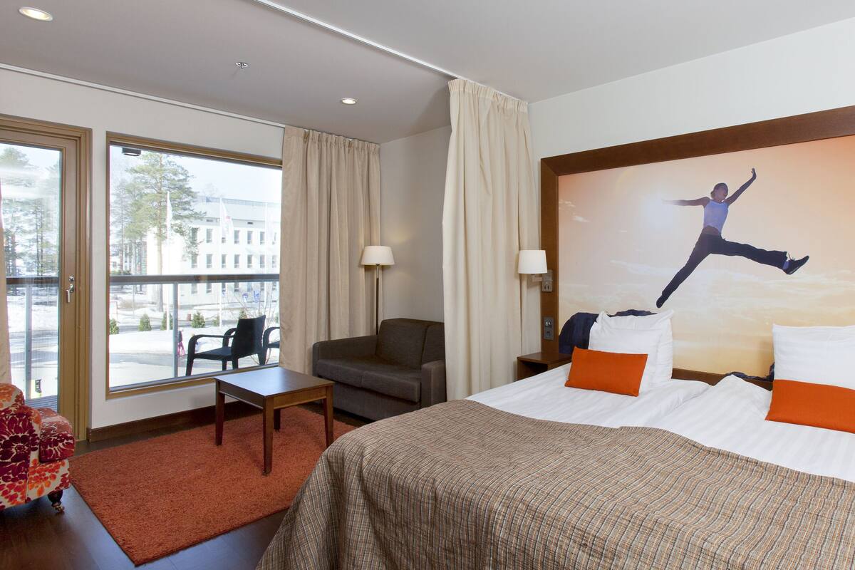 Une chambre d’hôtel avec un grand lit, un canapé, un bureau et une vue sur la ville par les fenêtres.
