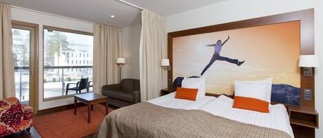 A hotel room with a large bed, a sofa, a desk, and a view of the city through the windows.