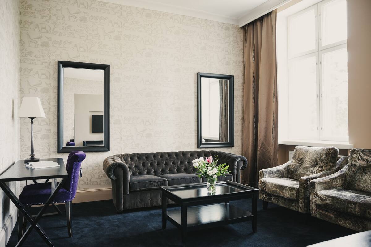 Une pièce avec un canapé marron foncé, un fauteuil assorti, une petite table sur laquelle est posé un vase de fleurs, et deux grands miroirs accrochés au mur.