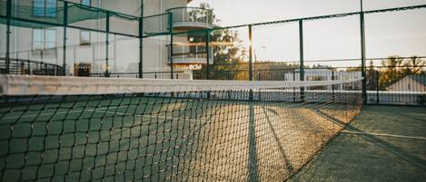 A tennis court with a net, surrounded by a building with a curved roof and glass railings.