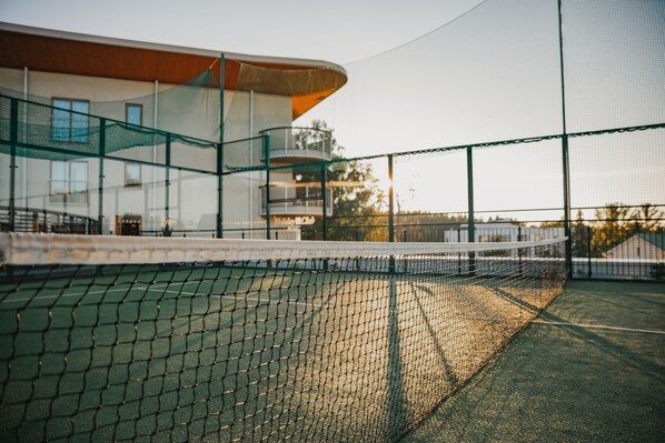 A tennis court with a net, surrounded by a building with a curved roof and glass railings.