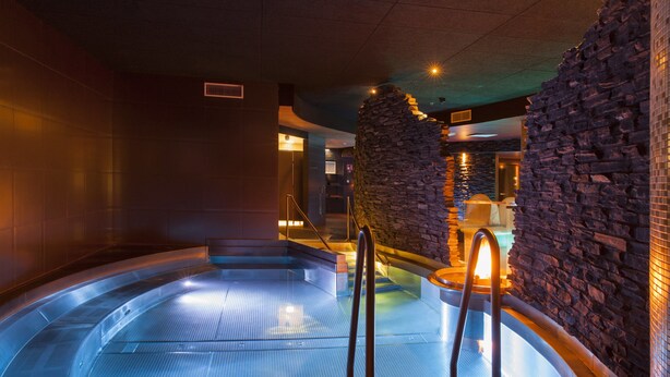 A hot tub area with a stone wall and wooden steps leading into the tub. - Holiday Club Saimaan Rauha (Lappeenranta)
