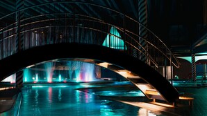 A modern indoor pool area with a curved glass bridge, water features, and ambient lighting. - Holiday Club Saimaan Rauha (Lappeenranta)