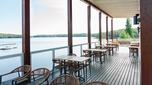 A covered outdoor seating area with tables and chairs, overlooking a body of water and forested hills. - Holiday Club Saimaan Rauha (Lappeenranta)