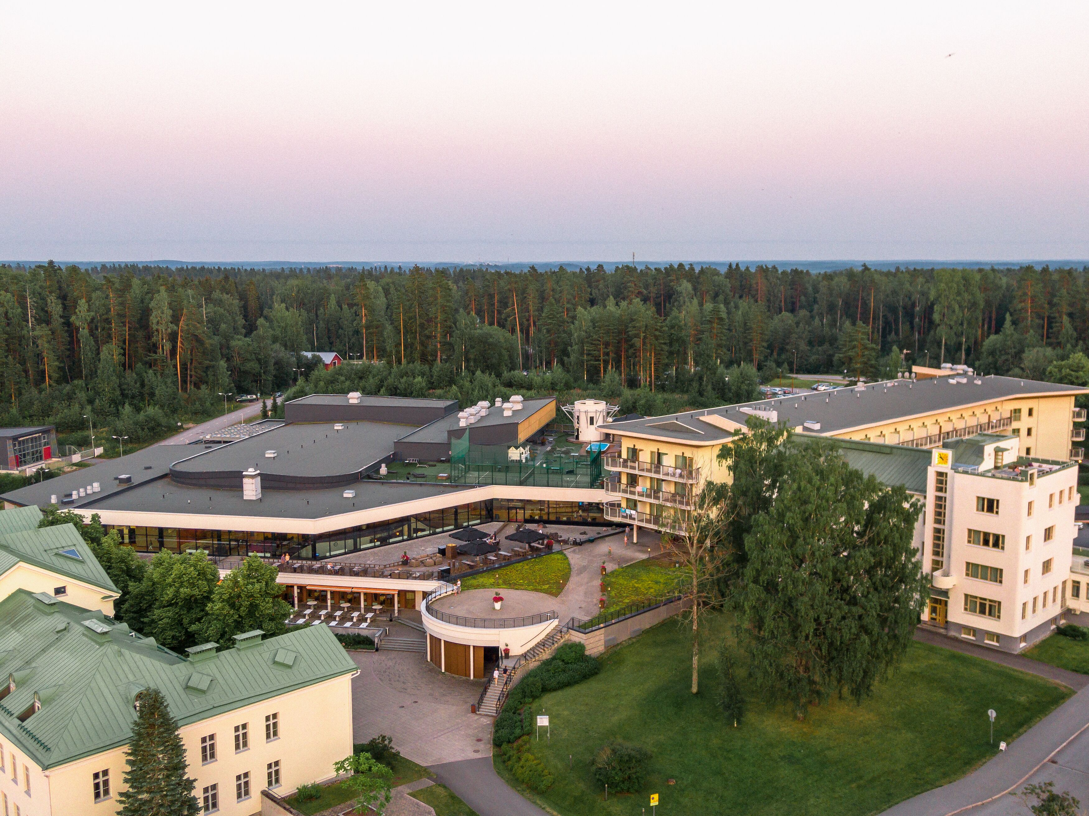 A hotel with a central courtyard, multiple buildings, and a surrounding forest.