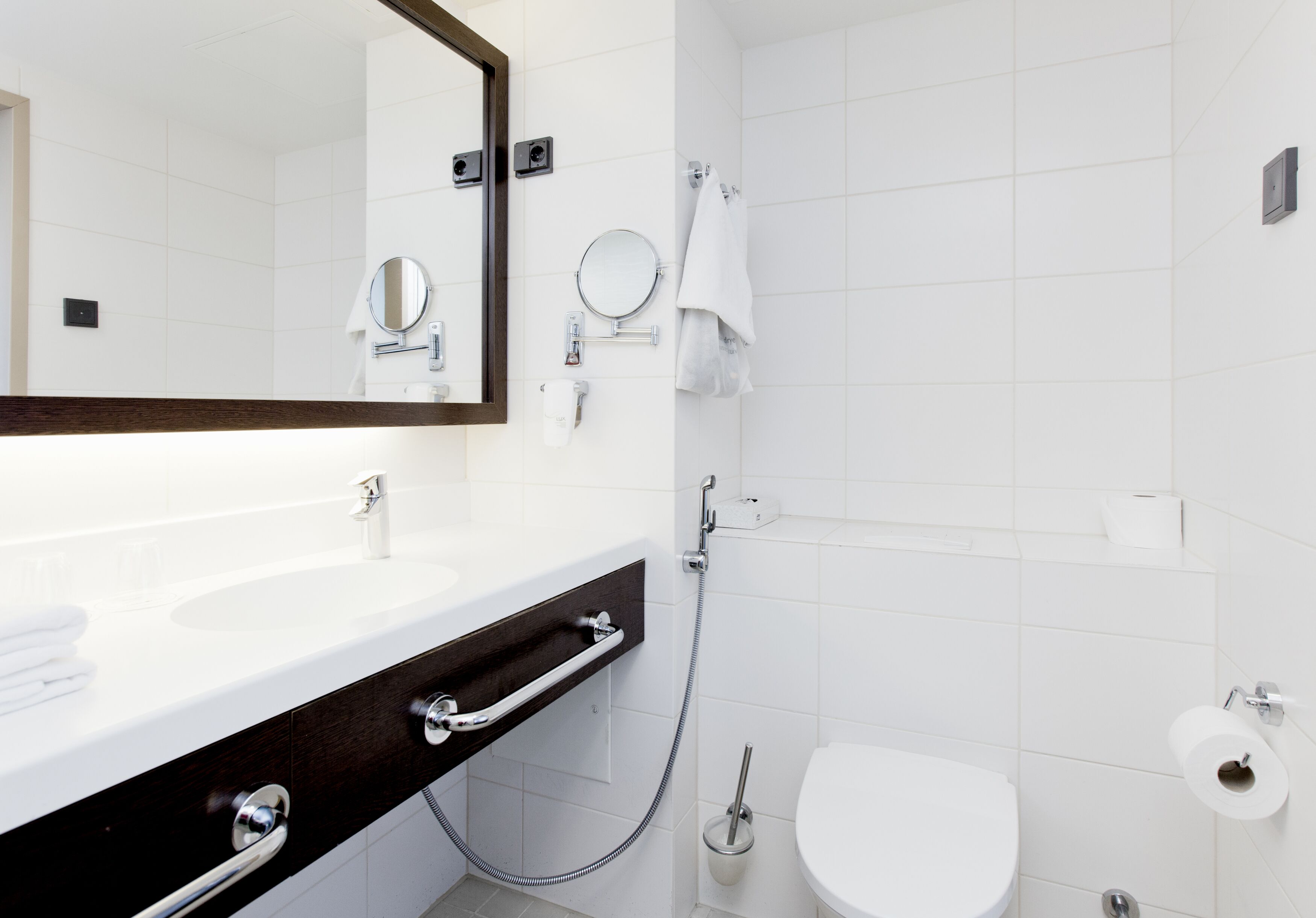A modern bathroom with a white sink, a mirror, a toilet, and a shower.