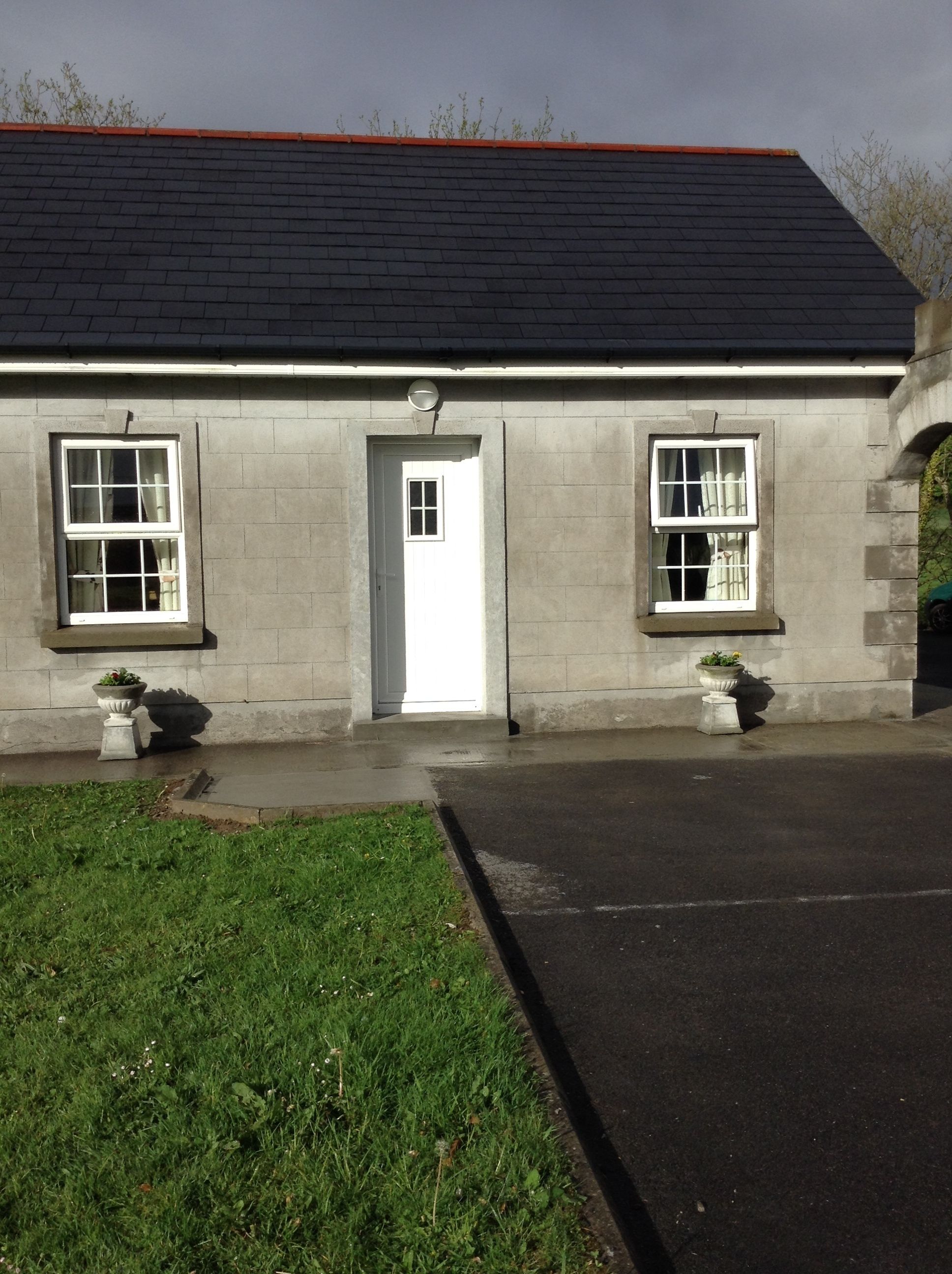 A two-story building with a dark roof, a white door, and two windows on the ground floor.