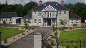 A large, two-story stone building with a symmetrical facade, a central entrance, and a landscaped front yard with a pathway leading to the entrance. - Deerpark Manor Bed & Breakfast (Swinford)