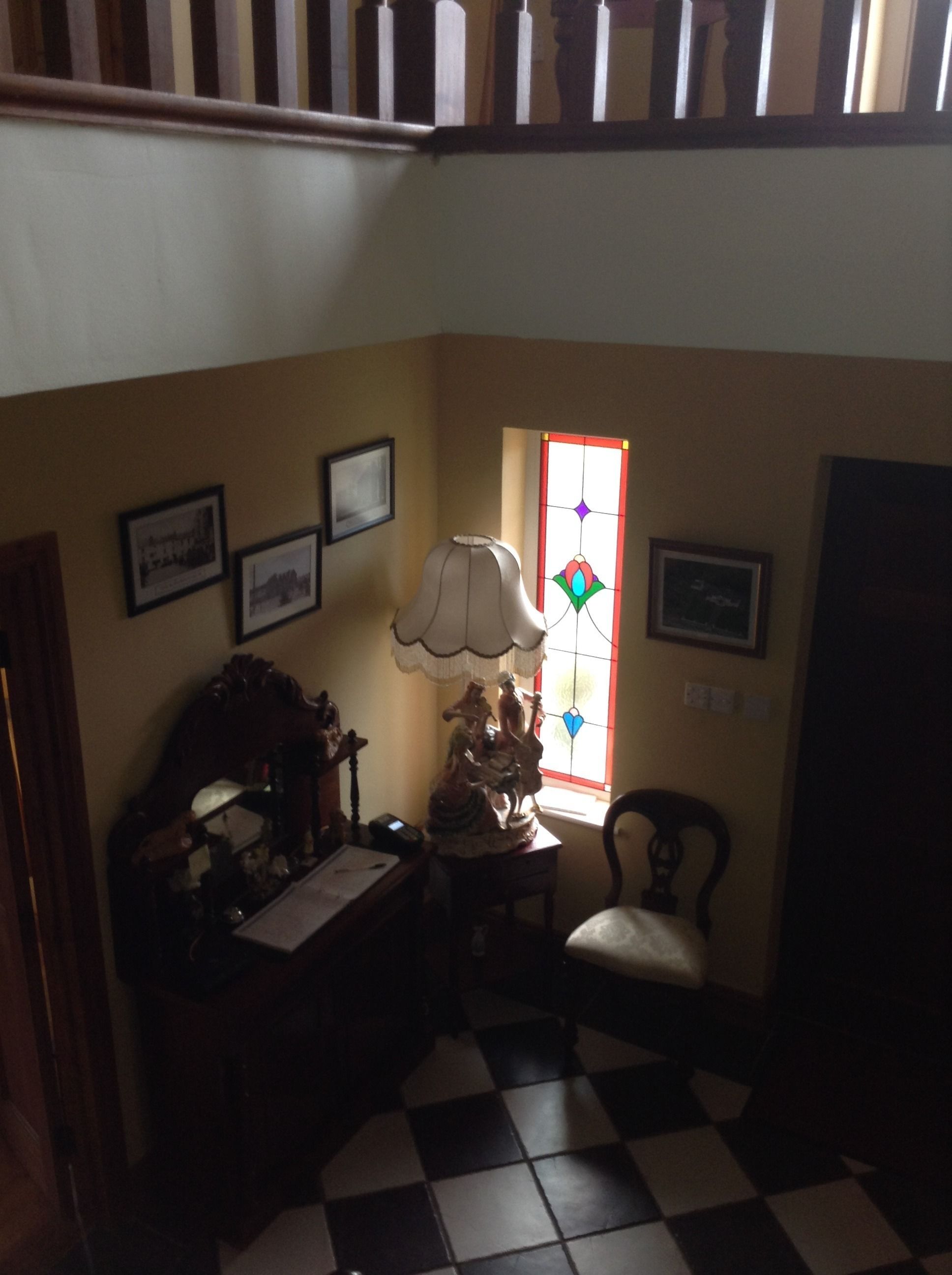 A room with a checkered floor, a desk with a lamp, a chair, and a window with stained glass.