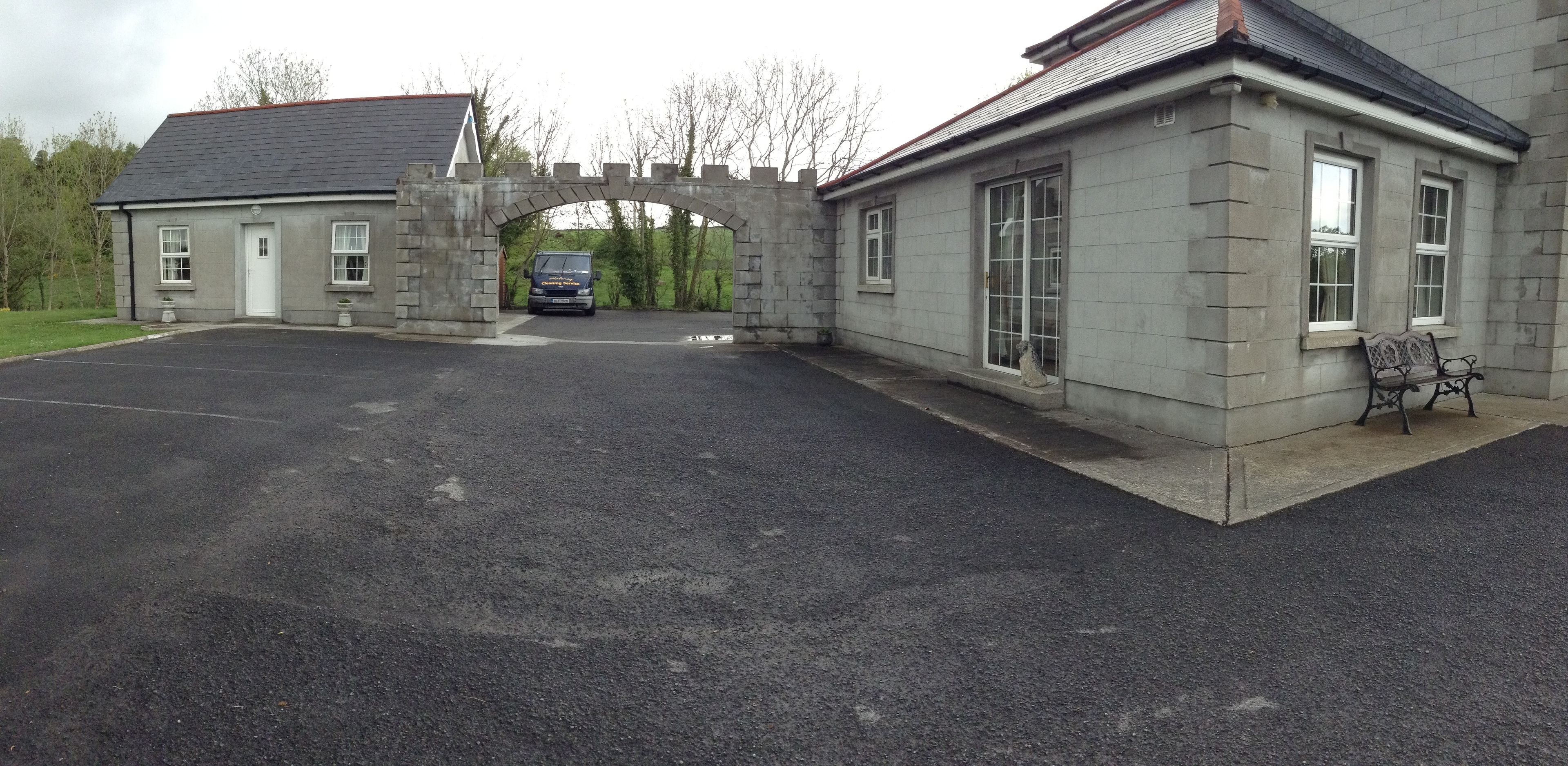 A stone building with a gated entrance, a bench outside, and a paved driveway.
