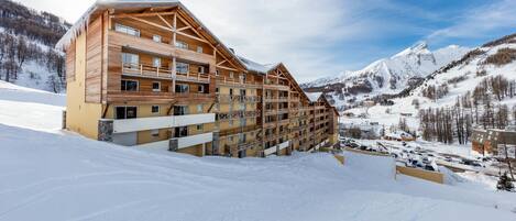 Un chalet en bois à plusieurs étages, doté de balcons, qui se dresse sur fond de montagnes enneigées.