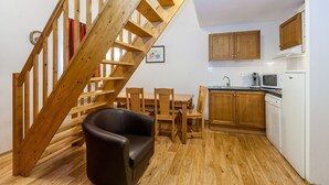 Una cocina con piso de madera, una mesa de comedor con sillas, una escalera con barandillas de madera y armarios de madera.