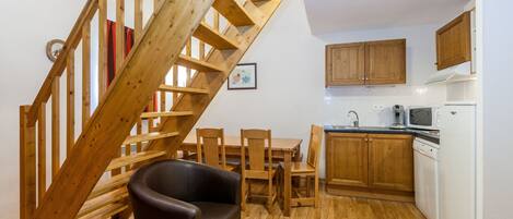 Una cocina con piso de madera, una mesa de comedor con sillas, una escalera con barandillas de madera y armarios de madera.