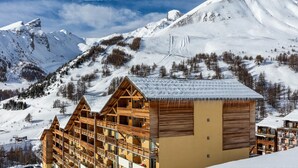 Un hotel de estilo chalet de madera, con varios balcones y una pista de esquí al fondo.