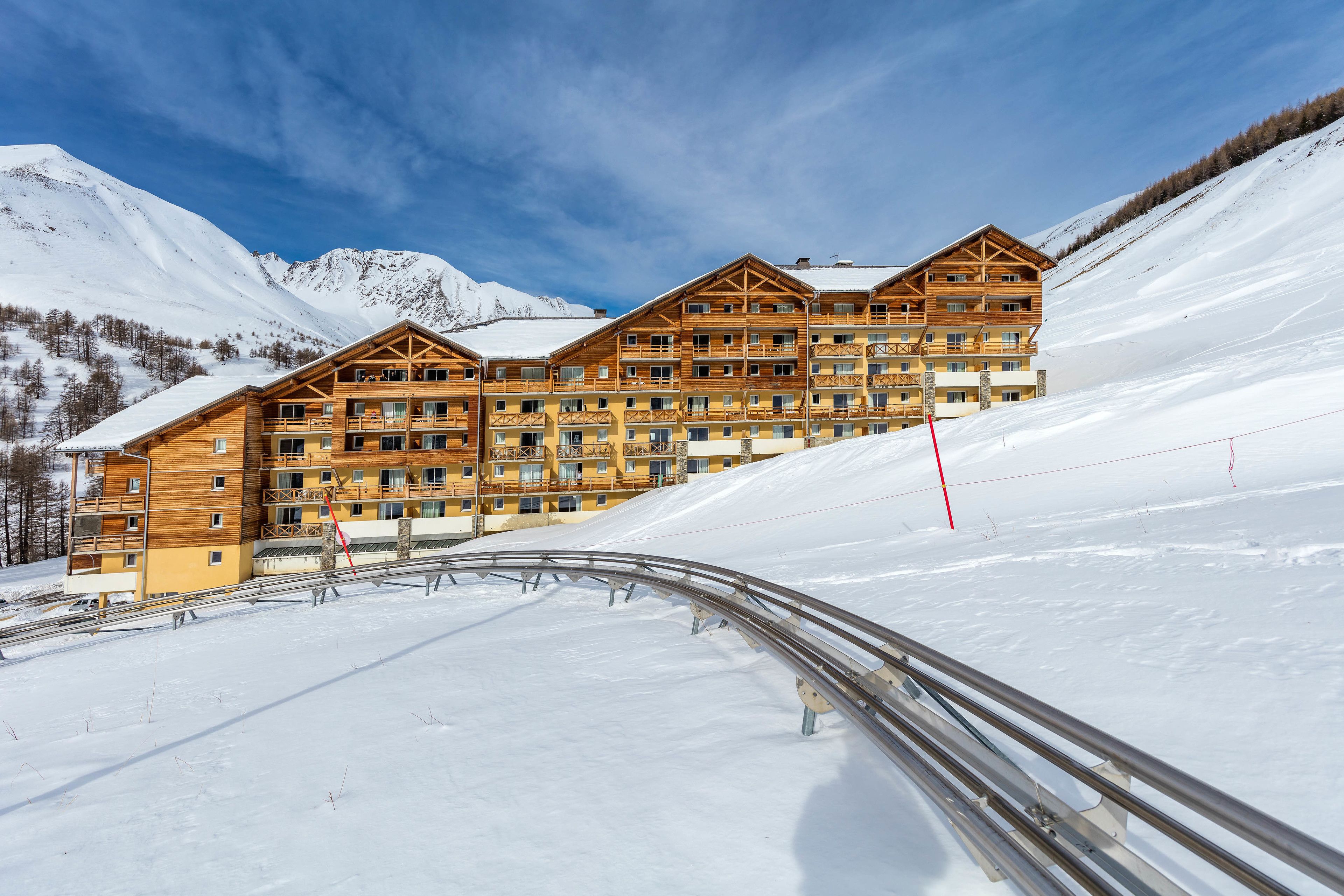 A wooden multi-story lodge with balconies, set against a snowy mountain backdrop.