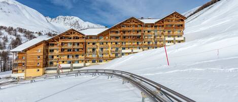 Una cabaña de madera de varios pisos con balcones, con una imponente montaña nevada de fondo.