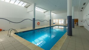 Una piscina interior con agua azul cristalina, paredes y suelo de baldosas.